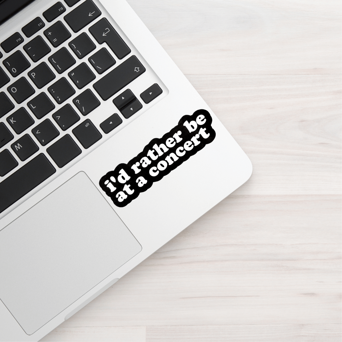 Laptop with a sticker saying 'I'd rather be at a concert' on a light wooden surface