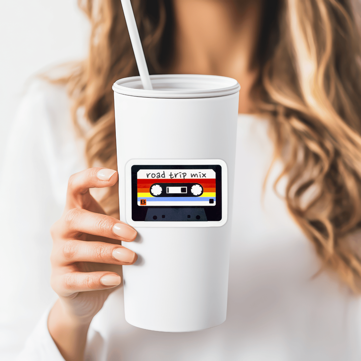 White tumbler with a 'road trip mix' cassette tape design held by a person.