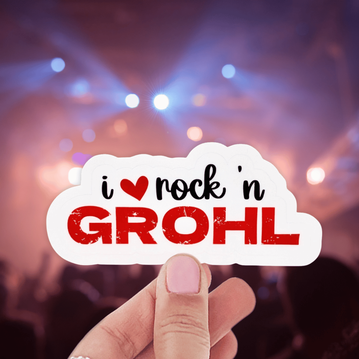 A person is holding a sticker that says "I love Rock n Grohl" on a blurred background that looks like a concert stage. The word Grohl is in a red distressed font and a red heart replaces the word "love"