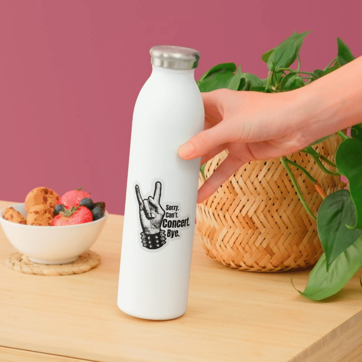 White water bottle with a black graphic and text held by a hand on a wooden surface with a bowl of snacks and plants in the background.