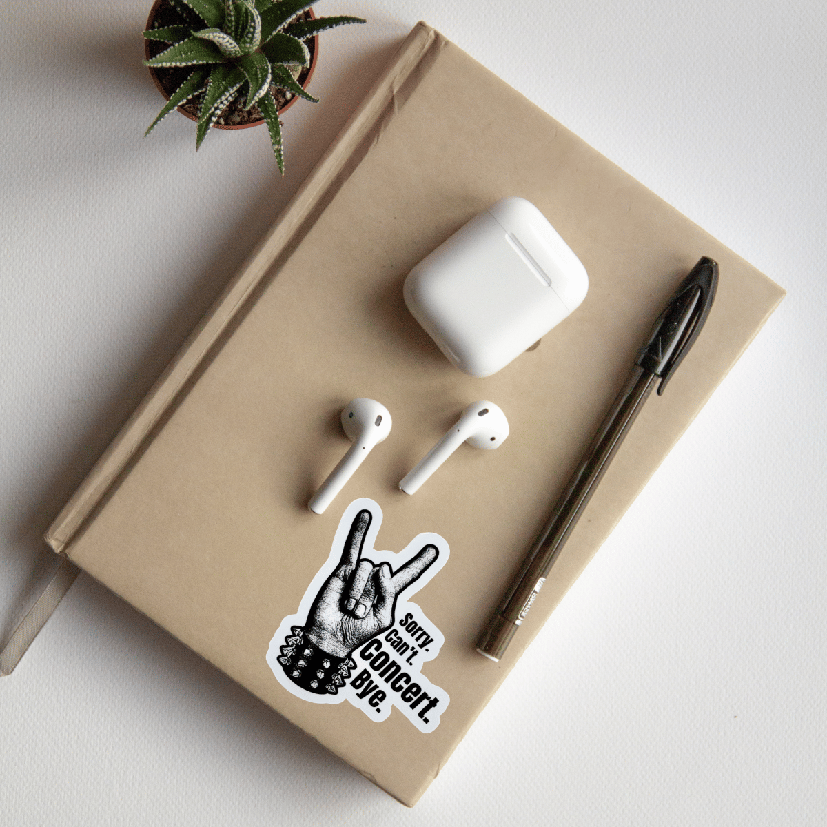 Notebook with AirPods, a pen, and a sticker on a light surface.