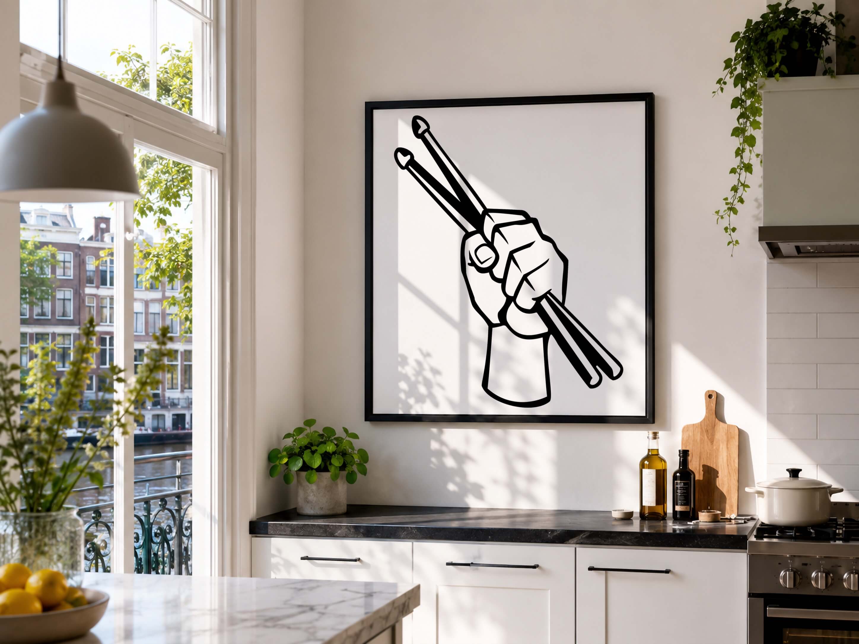 A framed black and white graphic art print of a hand holding drumsticks, displayed on a white kitchen wall above a counter with kitchen items.