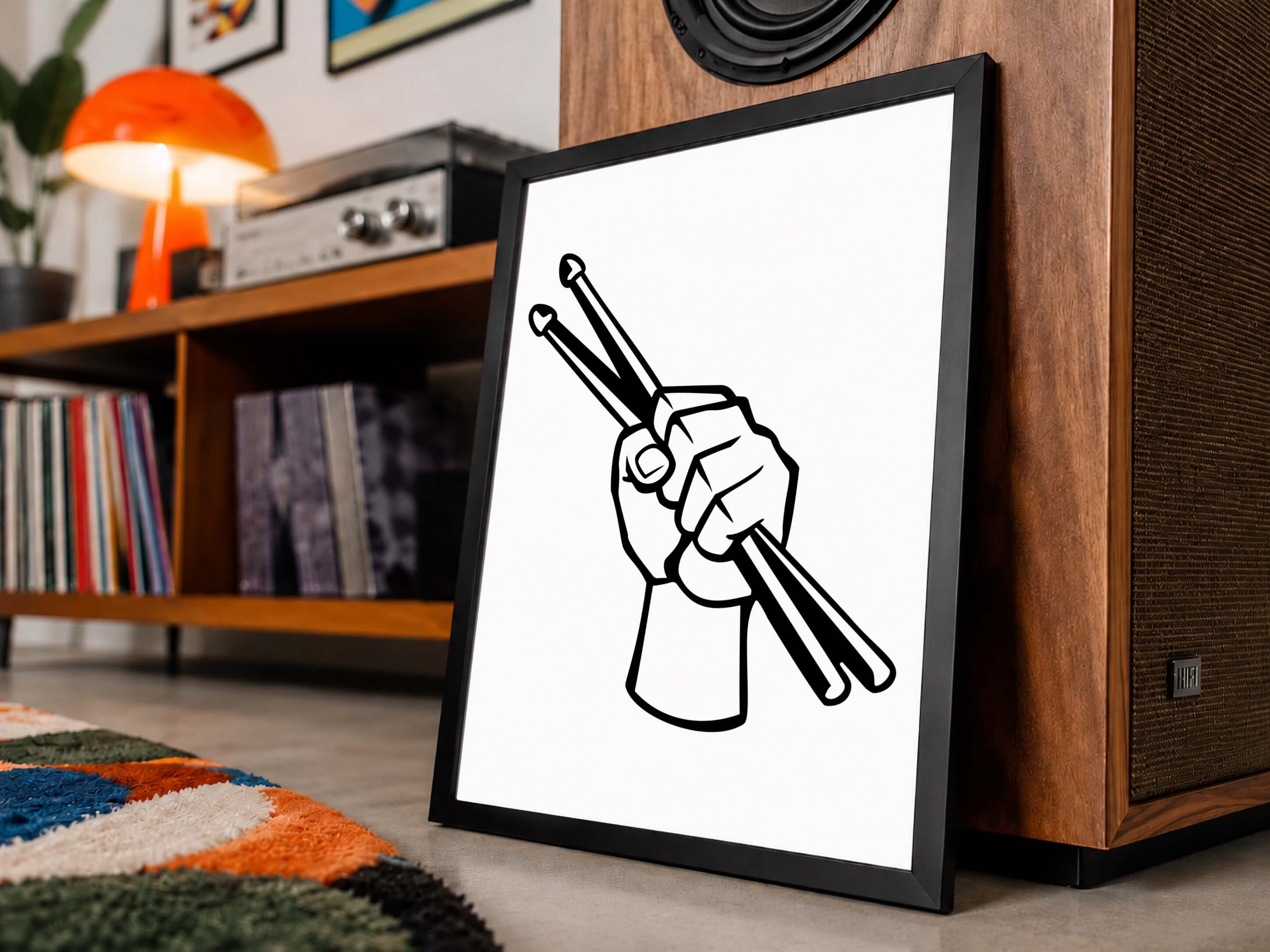 A framed black and white graphic art print of a hand holding drumsticks, leaning against a wooden speaker in a modern living room setting with records and a record player.