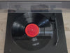 a record player is spinning, the lid on it shuts and a black, square, wood sign is placed on top. 