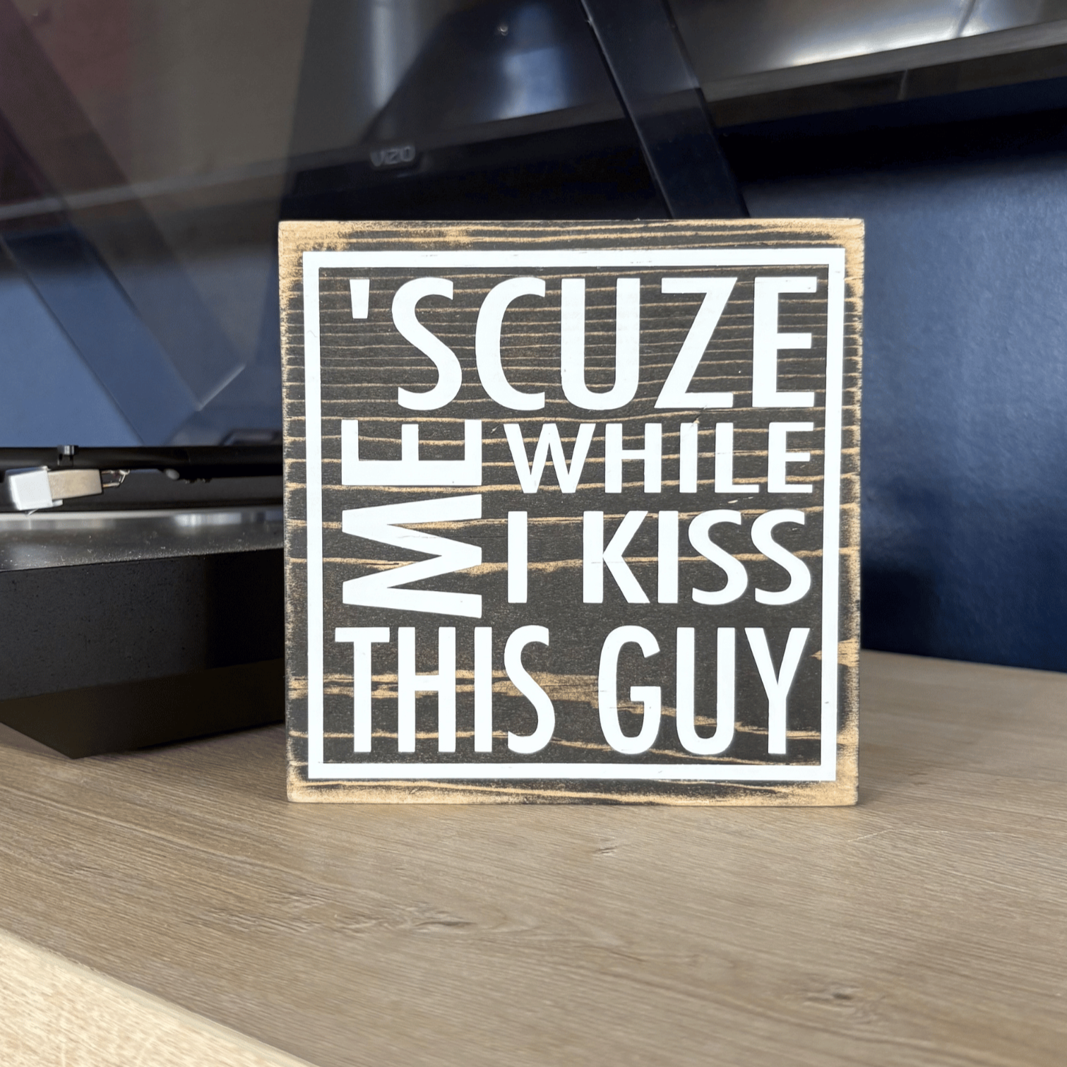 Wooden sign with humorous text on a shelf in front of a record player