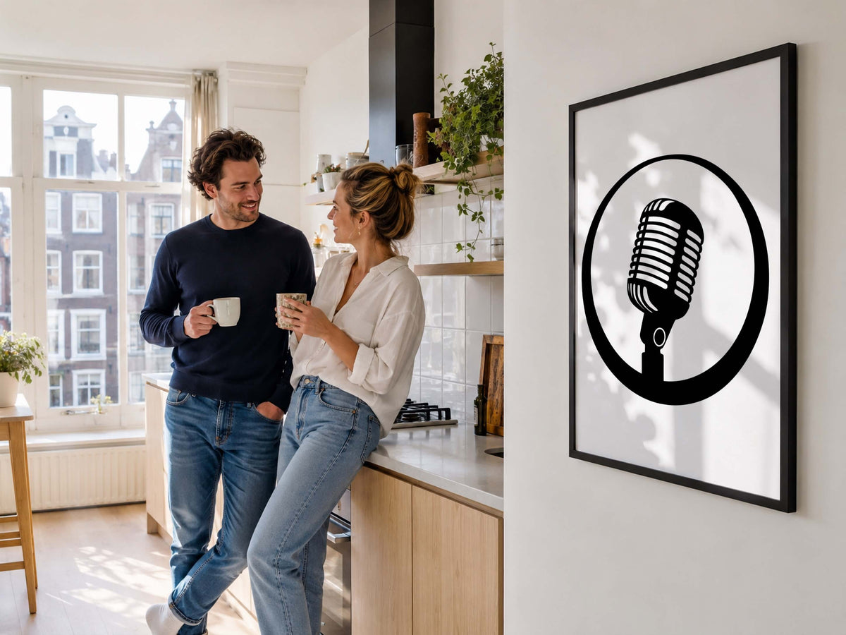 A framed black and white art print of a retro microphone hangs on a white wall in a modern kitchen where a couple is standing and holding mugs.