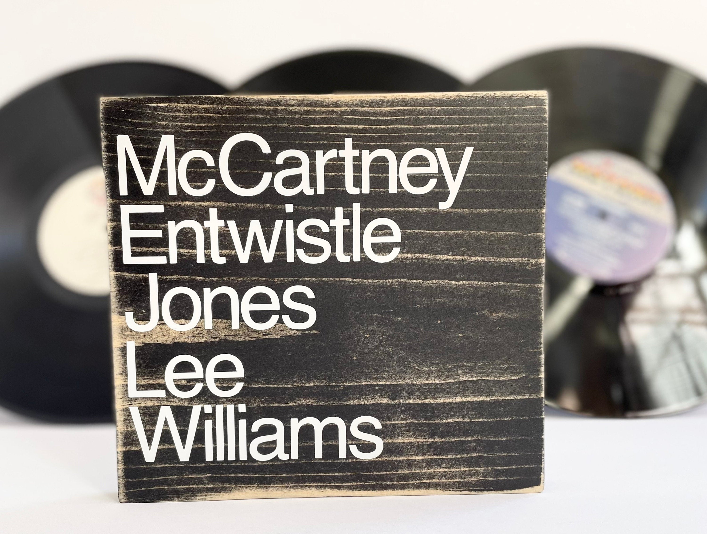 a square wood sign stained black with white, left justified, lettering that reads "McCartney Entwistle, Jones, Lee, Williams". The names are listed top to bottom.