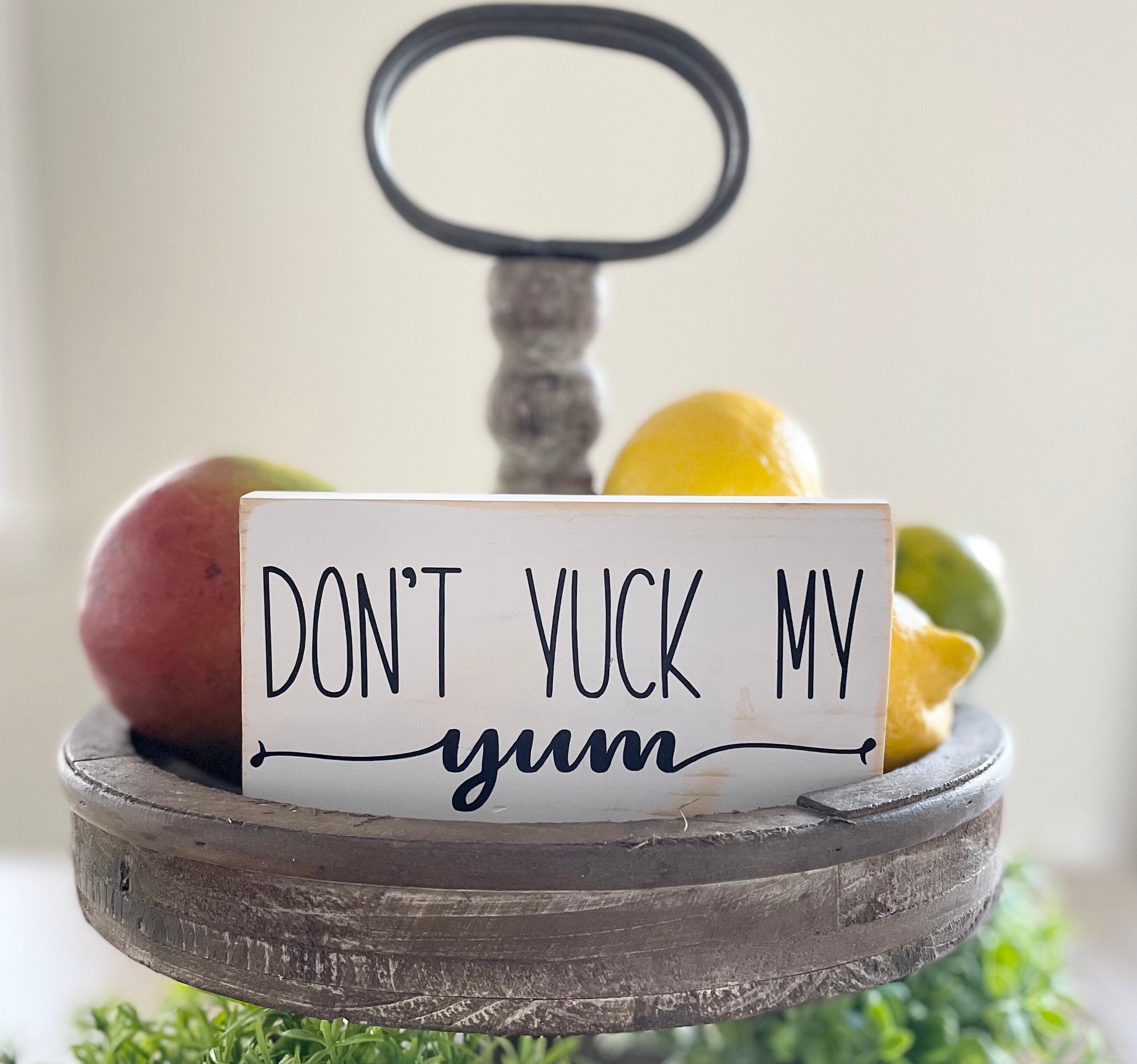 small wood rectangular sign painted white with black lettering that reads "Don't Yuck My Yum". Words are in all caps except for yum which is in a script font & is centered below the other words. The Y in yum has a "tail" that extends to the left, and the M in yum has a "tail" that extends to the right edge.