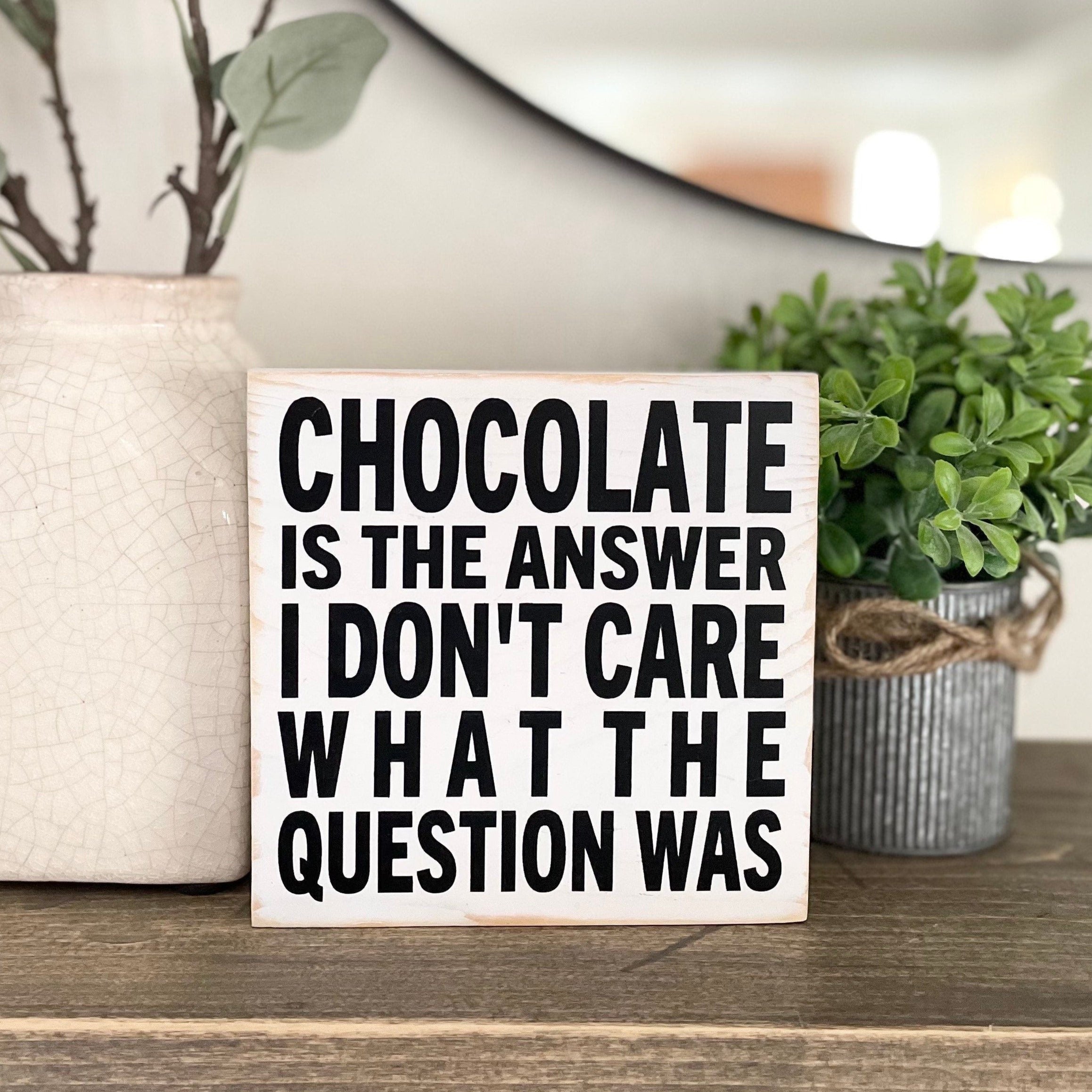 square, white wood sign with black lettering in all caps that says "Chocolate is the answer I don't care what the question was"