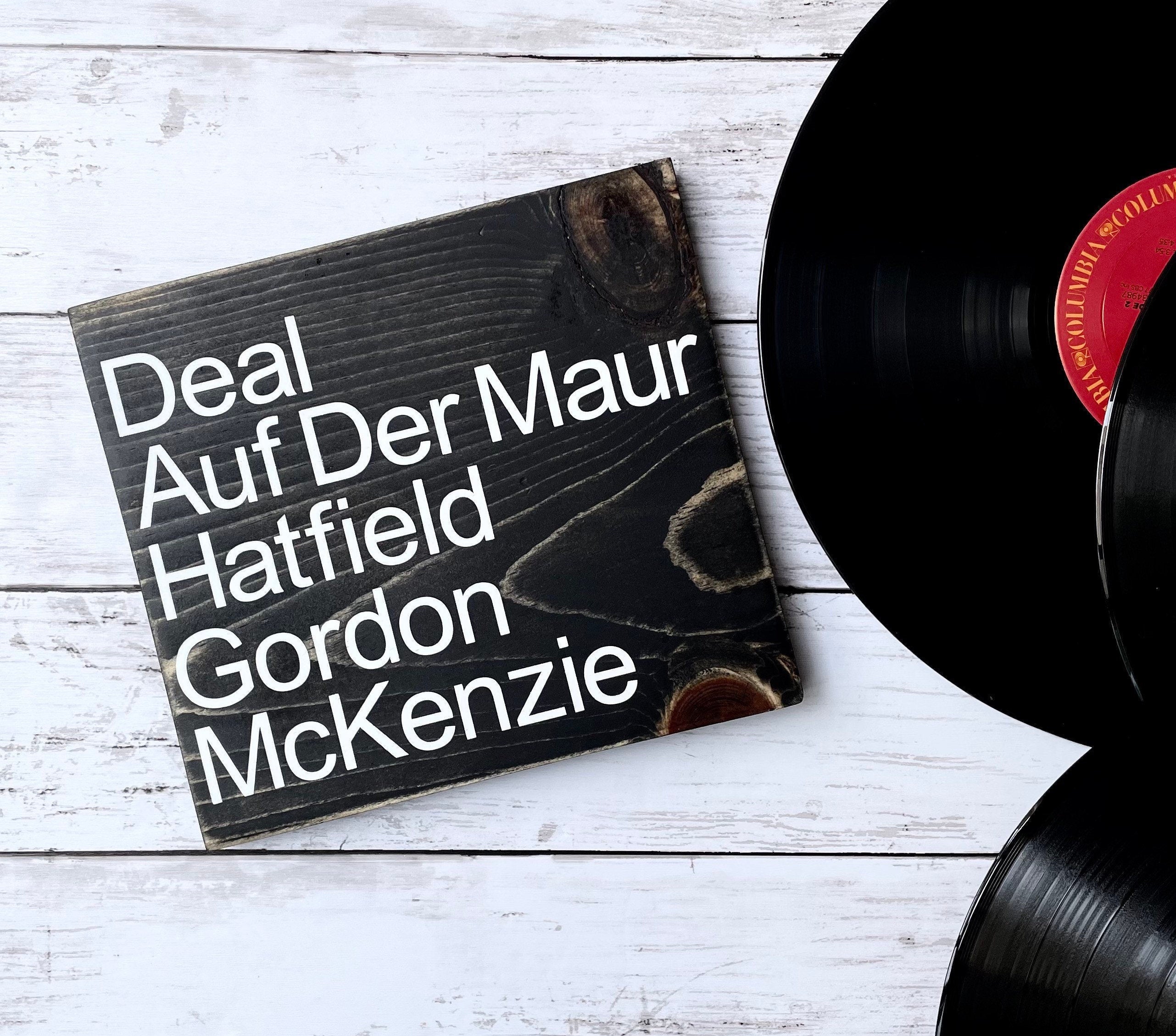 a square wood sign stained black with white, left justified, lettering that reads "Deal Auf Der Maur Hatfield Gordon McKenzie". The names are listed top to bottom.