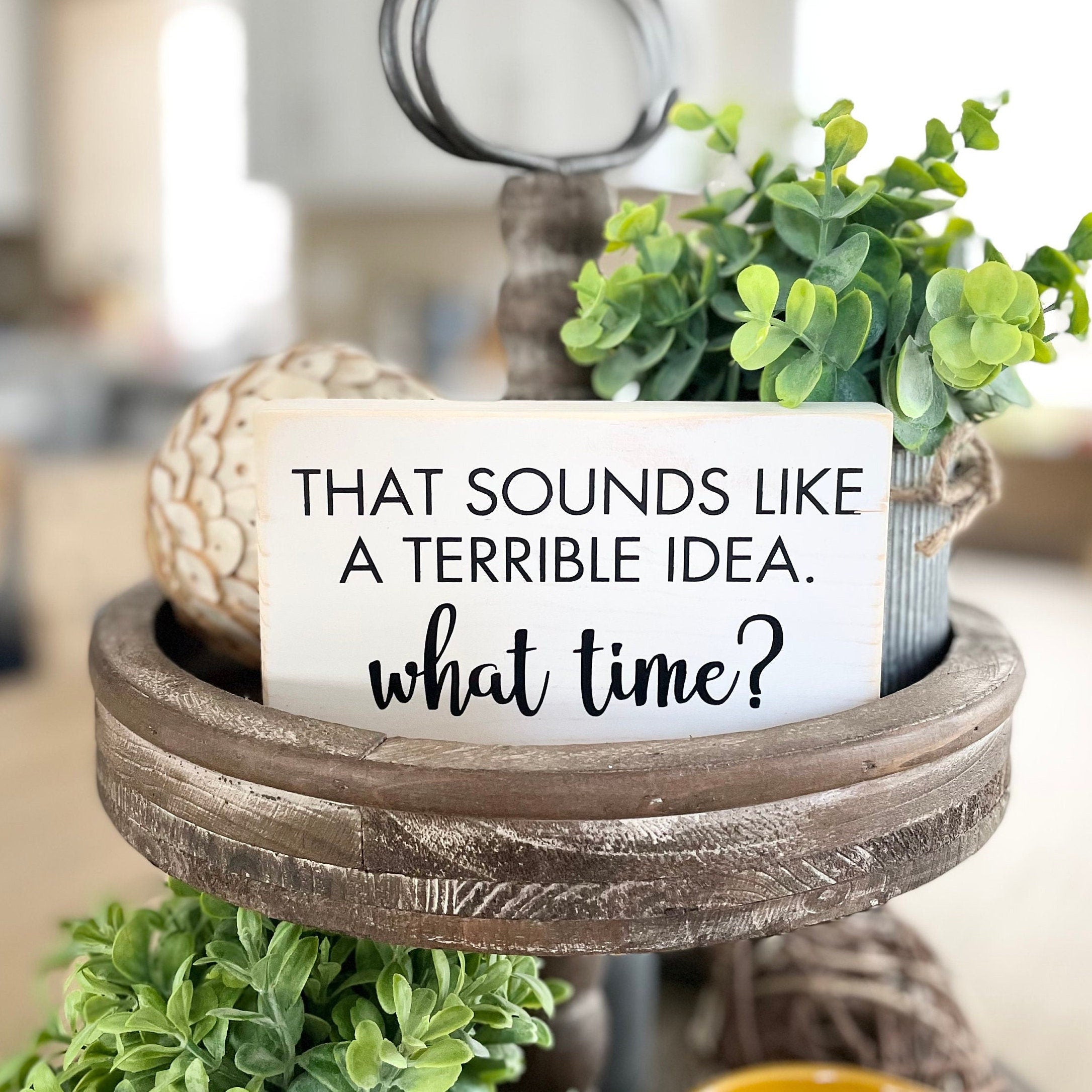 small wood rectangular sign painted white with black lettering that reads "that sounds like a terrible idea. What time?" All text is in all caps except for "what time?" which is in a script font