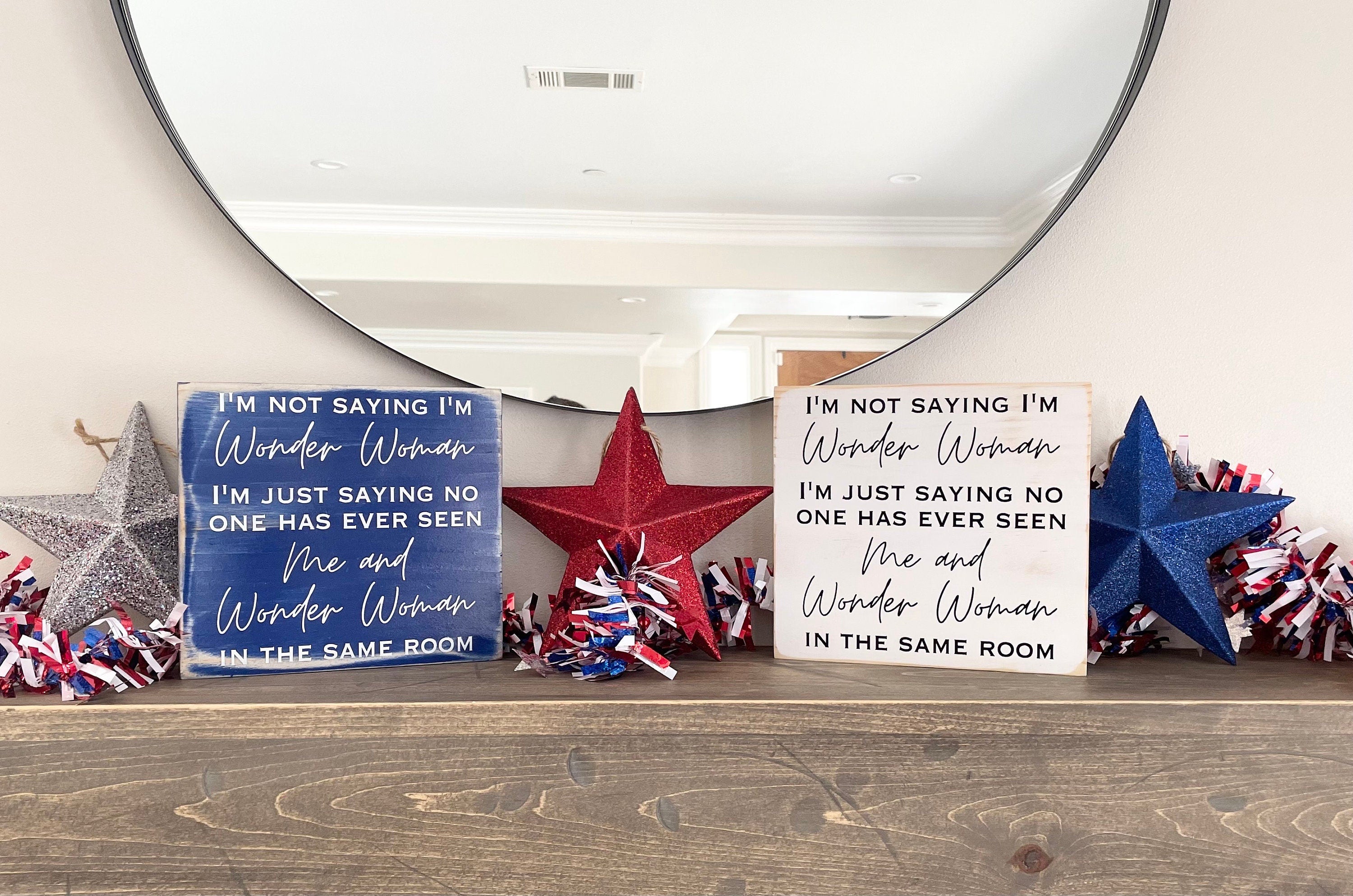 Two Wonder Woman signs sitting side by side on a mantle. The one on the left is blue, on the right is white