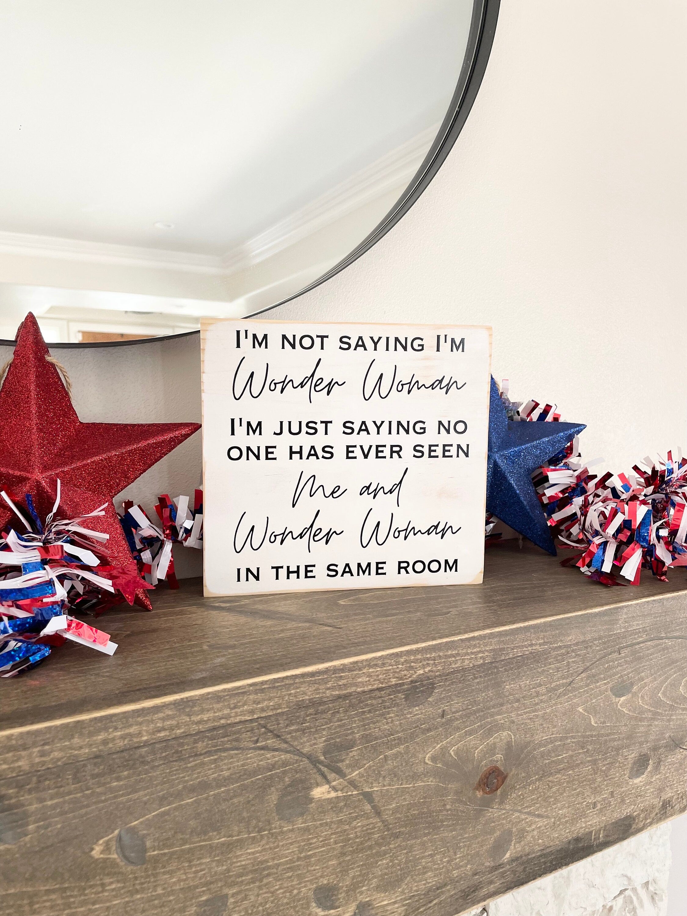 medium sized square wood sign painted white with black lettering that reads, " I'm not saying I'm Wonder Woman, I'm just saying no one has ever seen me and Wonder Woman in the same room". All text is in all caps except for "Wonder Woman" and "Me and Wonder Woman". Text is centered, takes up the entire area and is on 7 lines. Glossy finish.