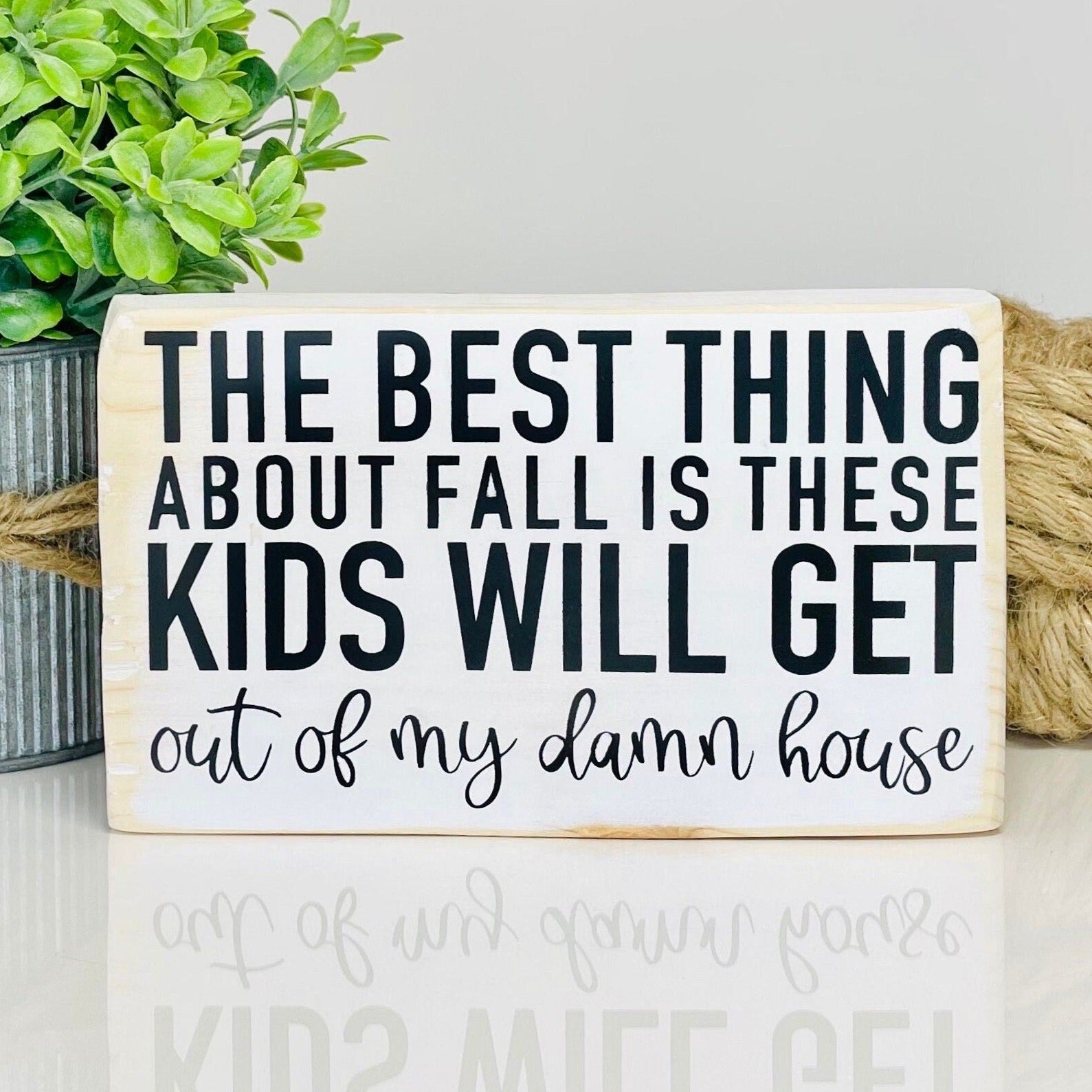 white rectangular small wood sign with black lettering that says "the best thing about fall is these kids will get out of my damn house". All words are in all caps except for "out of my damn house" which is in a script font